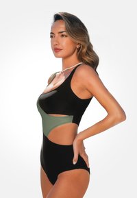 Zwart en olijfgroene badpak met uitsnijdingen, naadloze randen en een aansluitend ontwerp. Gladde textuur en verstelbare bandjes.