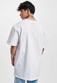 Balta medvilnės per didelė t-shirt su trumpomis rankovėmis ir apvaliu kaklu, pasižyminti lygiu paviršiumi ir patogiu kirpimu.