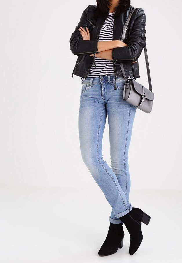 Giacca di pelle nera, t-shirt a righe, jeans chiari attillati e stivaletti neri con tacco. Borsa a tracolla grigia con cinturino.