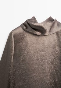 Haut marron texturé avec un col drapé, présentant un tissu froissé et une surface lisse et brillante. Le design comprend des manches longues et une coupe décontractée.