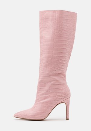 Botte stiletto rose montant jusqu'au genou avec bout pointu et texture crocodile embossée sur un matériau lisse sur fond blanc.