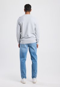 Gray textured sweater with long sleeves, paired with light blue denim jeans and white sneakers. Viewed from the back.
