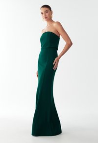 Zielona sukienka bez ramiączek wykonana z gładkiej tkaniny, z dopasowanym gorsetem i rozkloszowanym dołem. Charakteryzuje się elegancką sylwetką z minimalną ilością detali.