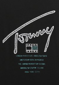 Czarny bawełniany t-shirt z białym, teksturowanym logo "Tommy". Zawiera nazwy miast w kolorze turkusowym oraz logo "TOMMY JEANS" w kwadracie.