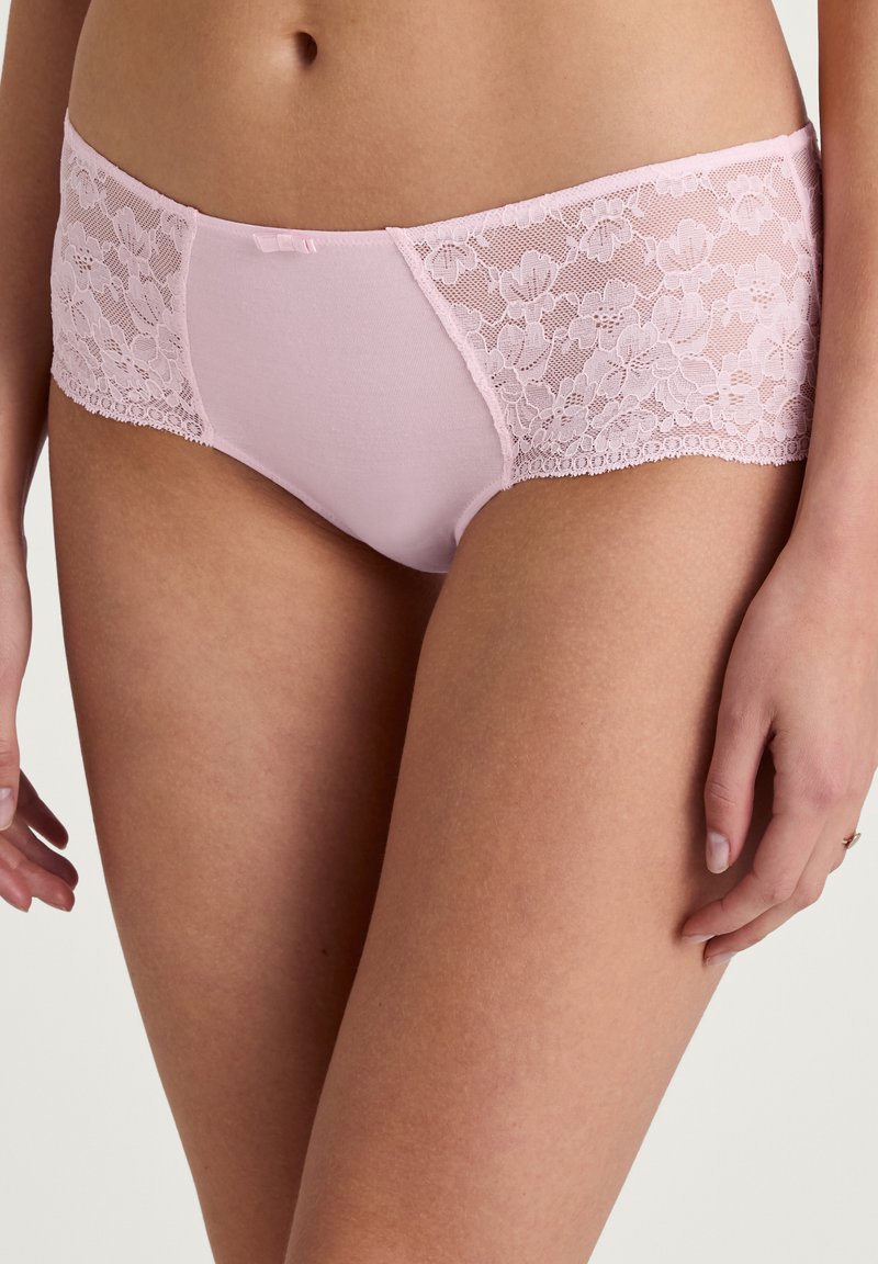 Lichtroze slipjes met een effen voorkant en kanten zijpanelen met bloemmotief, afgewerkt met een delicate kantafwerking en een klein strikje.