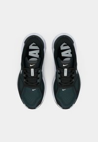 Chaussures de sport noires et vert foncé avec dessus en mesh, semelle blanche et marquage Nike bien visible en couleurs contrastantes sur la languette et la doublure intérieure.