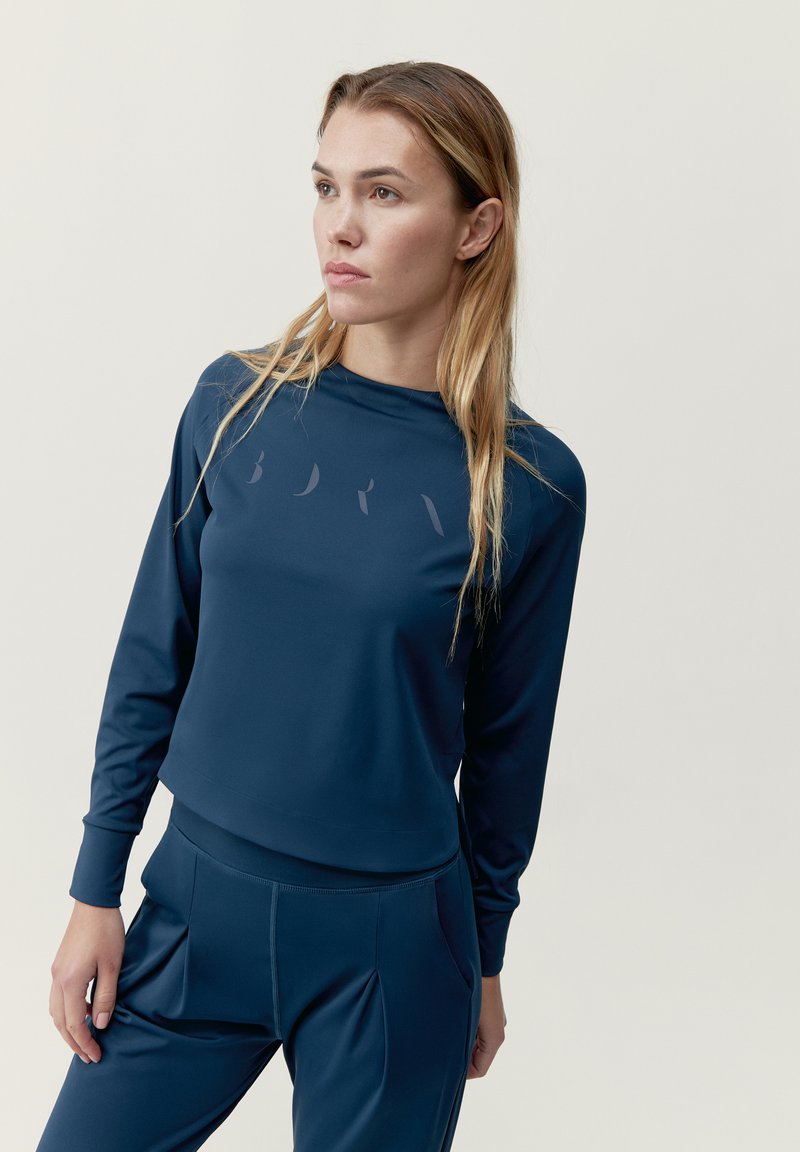 Marineblå långärmad träningsblus med rund halsringning, slät tyg, diskret logotyp på framsidan, tillsammans med matchande byxor med veck.