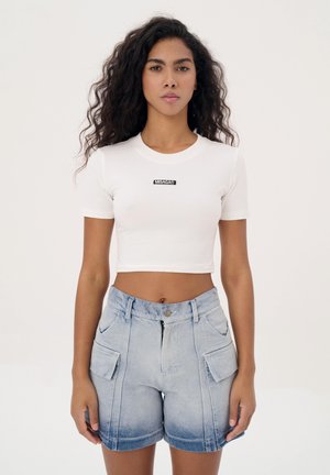 Witte katoenen crop top met korte mouwen, met een zwart "MISAGA" logo. Gepaard met lichtblauwe denim shorts met voorkruispockets.
