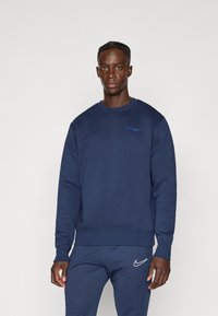 Sudadera azul marino con una textura suave, cuello redondo y mangas con puños. Presenta un logo bordado en azul en el pecho.