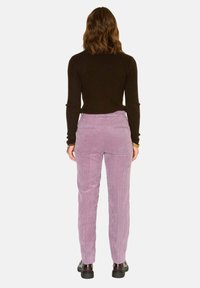 Pantalons en velours côtelé lilas avec des côtes verticales, poches arrière et une coupe légèrement taille haute, associés à un haut noir à manches longues. Chaussures noires.