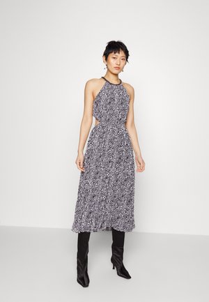 Rochie cu guler halter, în alb și negru, cu decupaje la talie și fustă fluidă, combinată cu cizme negre cu toc stiletto până la genunchi.