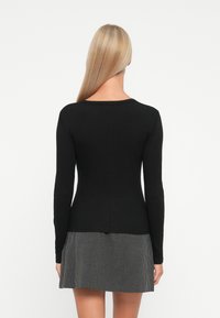 Haut à manches longues noir en ribbed avec un col rond, associé à une jupe à carreaux noir et blanc. Texture lisse, design ajusté.