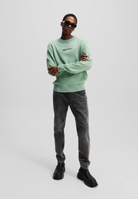 Mintgrøn strikket sweater med ribbede mansjetter og kant, logo på brystet. Sorte, slim-fit jeans og kraftige sorte støvler fuldender outfittet.