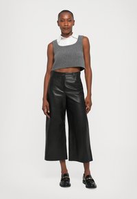 Grå stripete cropped genser, hvit skjorte med krage under, svart lær brede bukser. Svart loafers med gullakksenter.