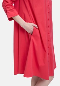 Robe rouge à manches longues avec boutonnage, dotée d'une poche latérale, texture douce et silhouette évasée.