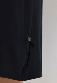 T-shirt in cotone nero con taglio dritto, maniche corte, spacchi laterali e una piccola etichetta vicino all'orlo con testo bianco su sfondo nero.