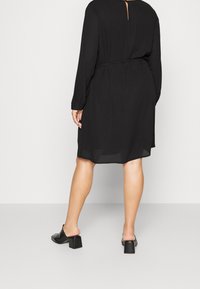 Svart långärmad klänning med cinchade midja, featuring en öppen rygg med ett nyckelhål. Kombinerad med svarta blockklackar.