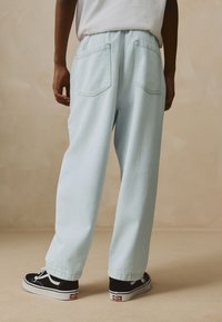 Hellblaue Jeanshose mit lockerem Schnitt, zwei Gesäßtaschen und umgeschlagenen Säumen. Kombiniert mit schwarz-weißen Canvas-Schuhen.