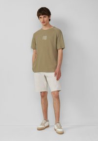 Jasnooliwkowy t-shirt z okrągłym dekoltem i krótkimi rękawami, w połączeniu z białymi szortami. Casualowe białe sneakersy z beżowymi akcentami.