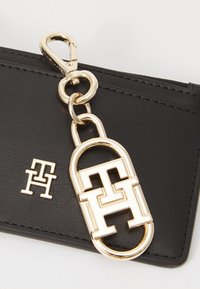 Sort læder tegnebog med en guld metal kæde og klips. Har et fremtrædende guld låseformet logo og et mindre logo ved siden af.