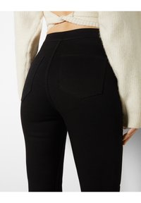 Zwarte hoge taille jeans met een gladde textuur, slim fit en twee achterzakken met hoekige ontwerpen. Gepaard met een lichtgekleurde trui.