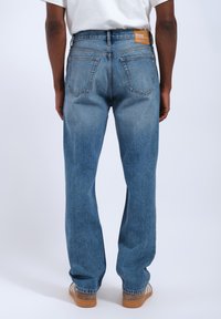Jeans in denim azzurro chiaro con una vestibilità a gamba dritta, cuciture visibili e una toppa in pelle sulla vita posteriore. Due tasche posteriori visibili.