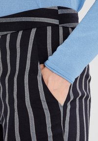 Navyrandiga byxor med vita vertikala linjer, med en ficka. Bärs med en ljusblå långärmad tröja, med synlig textur.