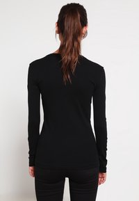 Svart långärmad skjorta med en figurnära design och mjuk textur, med rund halsringning och minimala sömdetaljer på baksidan.