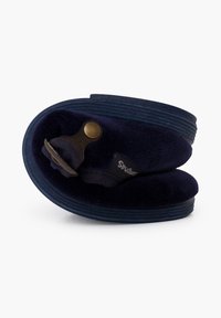 Zapatilla de color azul marino con forma redondeada, hecha de material suave, que presenta un cierre de metal y una suela texturizada. Incluye una etiqueta con logo.