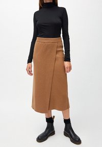 Brun stickad midi kjol med omslagdesign, ribbad midja och textilstruktur; ihop med en svart långärmad topp och svarta stövlar.