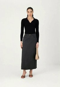 Blusa preta de manga longa com gola rasa, combinada com uma saia cinza escura até os tornozelos que apresenta uma costura diagonal e uma textura subtil.