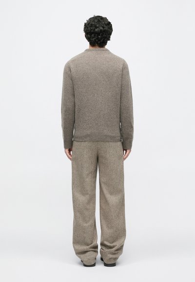 Maglione lavorato a maglia marrone con colletto rotondo, abbinato a pantaloni beige a vestibilità ampia, caratterizzati da un tessuto testurizzato e una cintura elastica.