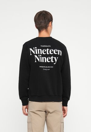Zwarte sweatshirt met grote witte tekst op de achterkant: "Opgericht in negentienhonderdnegentig" en "Ontworpen door het J&J-team." Zachte stof.