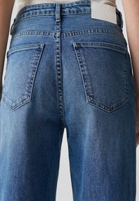 Blauwe spijkerbroek met een hoge taille, vijf zakken en een gestructureerde afwerking. Bevat een wit logo-opdruk op de achterkant van de tailleband.
