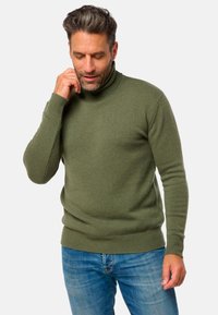 Pull à col roulé en rib vert foncé en tricot texturé. Manches longues et coupe ajustée, associé à un jean en denim bleu.