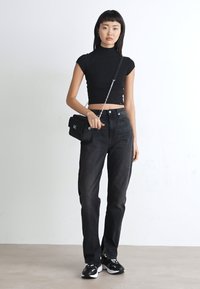 Top crop nero attillato, jeans scuri a vita alta, borsa a tracolla nera con manico a catena e sneakers nere con accenti bianchi. Design minimalista.