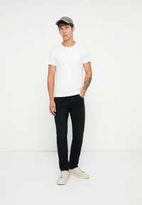 T-shirt bianco a maniche corte, jeans neri, berretto grigio e sneakers di colore chiaro. Design semplice e aderente senza pattern o grafiche visibili.
