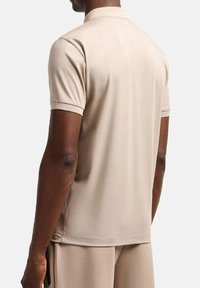 Polo shirt beige a maniche corte con una texture morbida, dotato di un colletto classico e una vestibilità rilassata, vista dal retro.