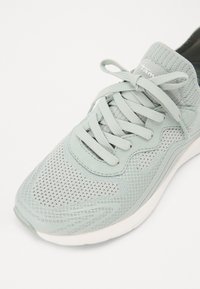 Light gray athletic sneaker with mesh upper, fabric laces tied in a bow, and thick white sole on a white background.