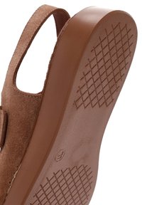 Zapato de ante marrón con tacón bajo, lados abiertos y suela de goma texturizada con un patrón de rejilla para mayor agarre.