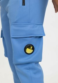 Pantalons cargo bleu ciel en tissu lisse, dotés d'une poche à rabat sur le côté et d'un accent métallique rond avec une lentille dorée réfléchissante.
