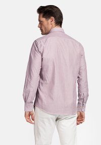 Chemise à manches longues rayée rouge et blanche avec un col standard, un ourlet arrondi, des poignets boutonnés et un tissu texturé. Détails de couture visibles.