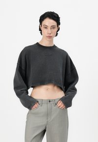 Felpa nera corta con maniche ampie e colletto a costine. Abbinata a pantaloni dritti grigio chiaro con tasche frontali.