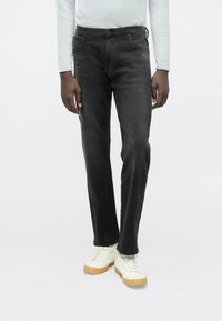 Μαύρο τζιν με ίσια γραμμή, πέντε τσέπες, ελαφριά ξεβάμματα και κλασικό κούμπωμα με κουμπιά, συνδυασμένο με λευκά αθλητικά παπούτσια και ανοιχτόχρωμο τοπ.