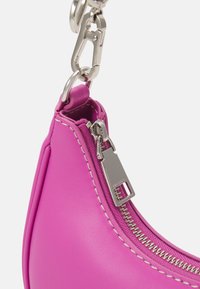 Pochette en cuir rose vif avec des coutures blanches, fermeture éclair argentée et fermoir argenté attaché sur fond blanc uni.