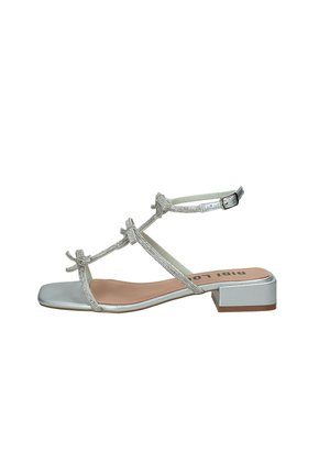 Sandalo argento con cinturini, tacco basso a blocco, tre fiocchi decorativi sulle cinghie anteriori e chiusura regolabile con fibbia alla caviglia.
