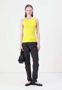Gul ribbet tank topp kombinert med mørk denim jeans, svarte flate sko og en liten svart håndveske. Enkelt design, tettsittende silhuett.