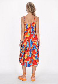 Farbenfrohes ärmelloses Kleid mit einem gestuften Design, das auf leichtem Stoff in leuchtenden Rot-, Orange-, Blau- und Gelbtönen mit abstrakten Mustern gestaltet ist.