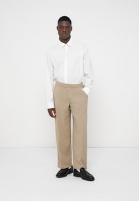 Weißes Langarmhemd mit Kragen, kombiniert mit beigen Karohosen. Schwarze Schuhe runden den smart casual Look ab. Einfaches und maßgeschneidertes Design.