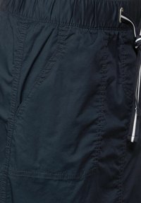Pantalones cortos azul marino hechos de un tejido ligero, con una cintura elástica y cordón, bolsillo lateral y detalles de costura visibles.